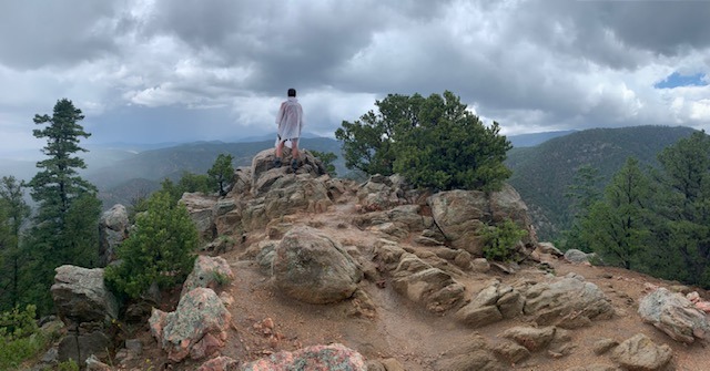 Kaity standing at the top of a mountain in New Mexico, her back is to the camera and she is looking at the sky.